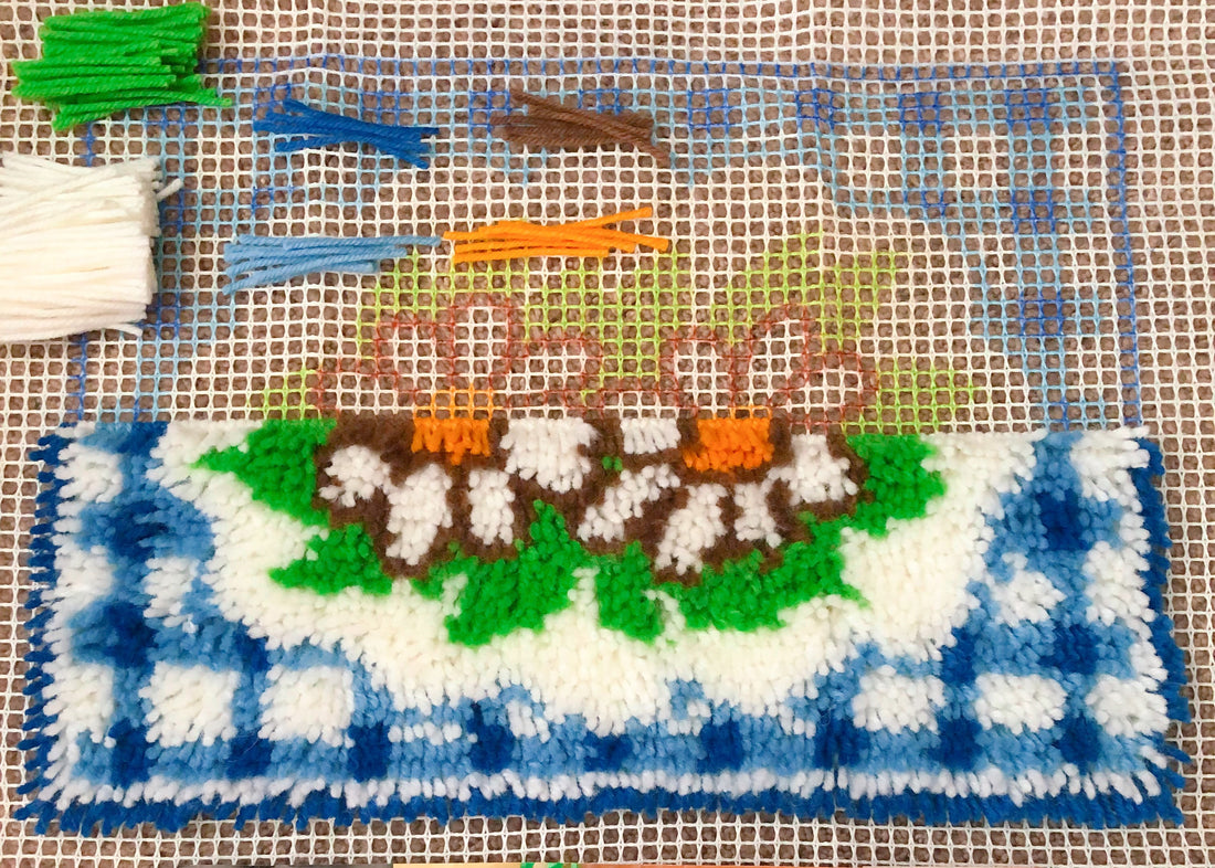 A half done latch hook pillow of white daises on a blue gingham background.