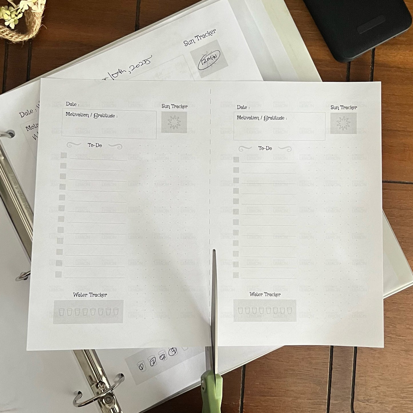 Person cutting a printed planner sheet with green scissors on a wooden surface.