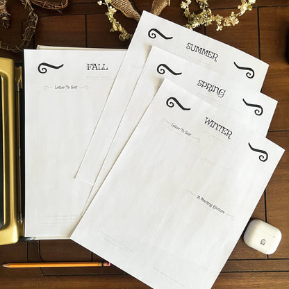 Four seasonal letterhead sheets on a wooden surface with decorative elements.